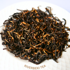 Dried black tea leaves with "golden tips" on a white plate with 'Riverbeki Tea' branding.